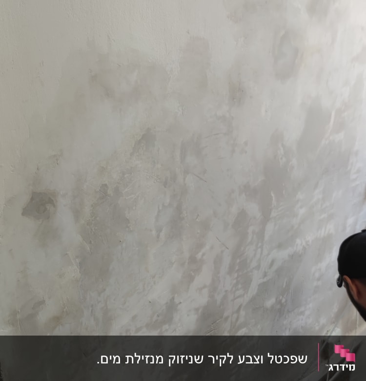 קיר עם טיח מתקלף ואדם עובד לידו